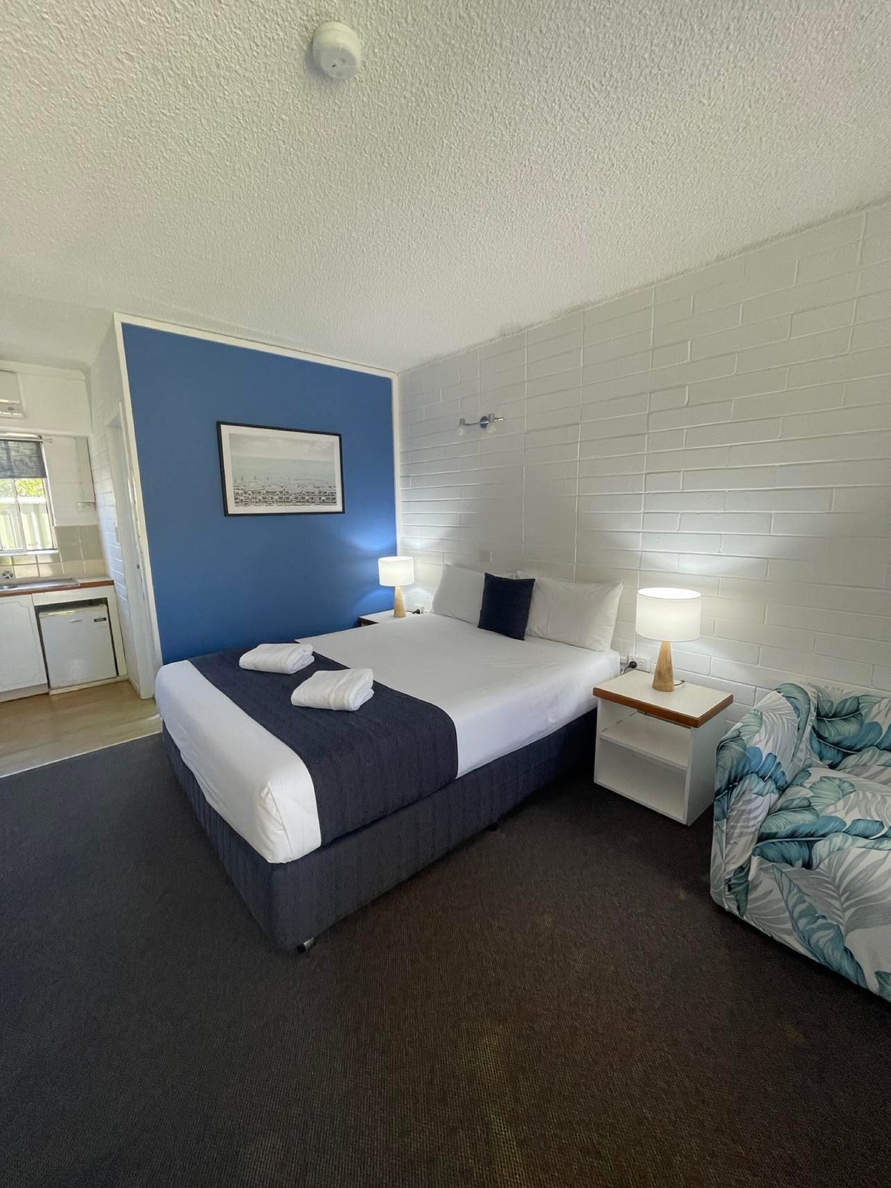 Une chambre d’hôtel avec un lit, une table de chevet, une lampe et une vue sur la cuisine.