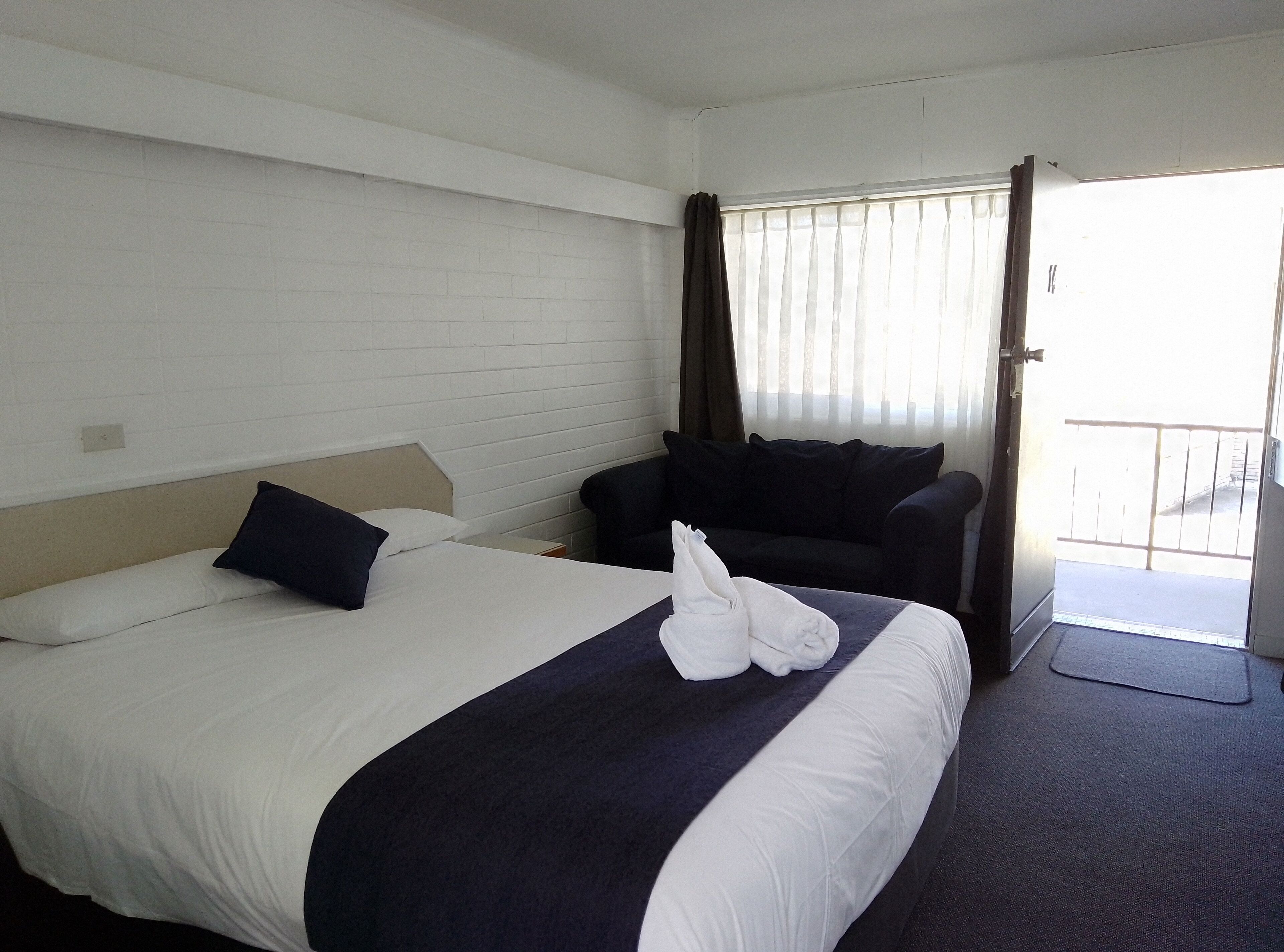 A hotel room with a bed, a sofa, a window with curtains, and a door leading to a balcony.