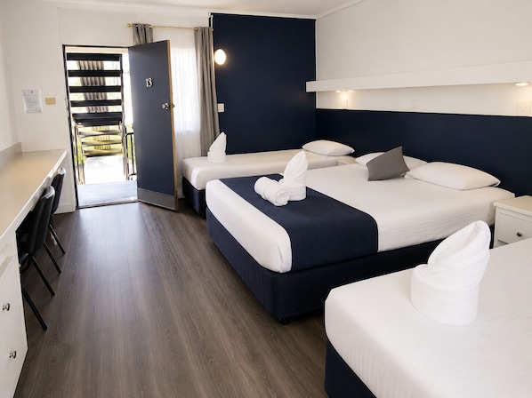 A hotel room with three beds, a desk, and a door leading to a balcony.