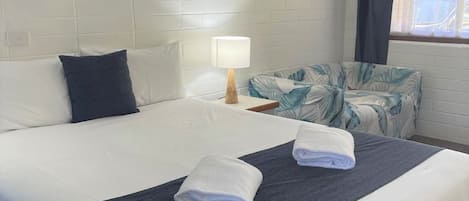 Une chambre d’hôtel avec un grand lit, une table de chevet avec une lampe, une fenêtre avec des rideaux et une vue sur l’extérieur.
