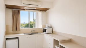 A compact kitchen with a window, a microwave, a sink, and a small refrigerator. - Forster Motor Inn (Forster)