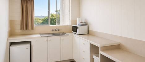 A compact kitchen with a window, a microwave, a sink, and a small refrigerator.