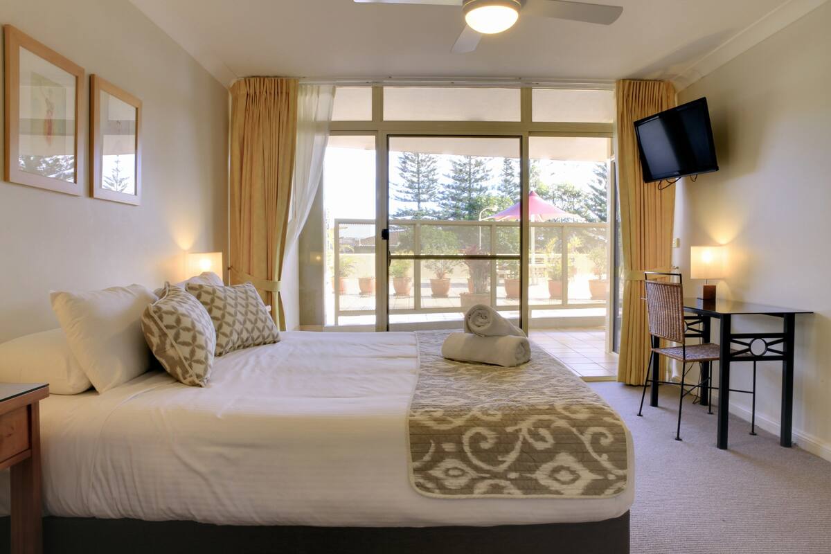 Habitación de hotel con una cama grande, un escritorio con una silla, un televisor y vistas al exterior.