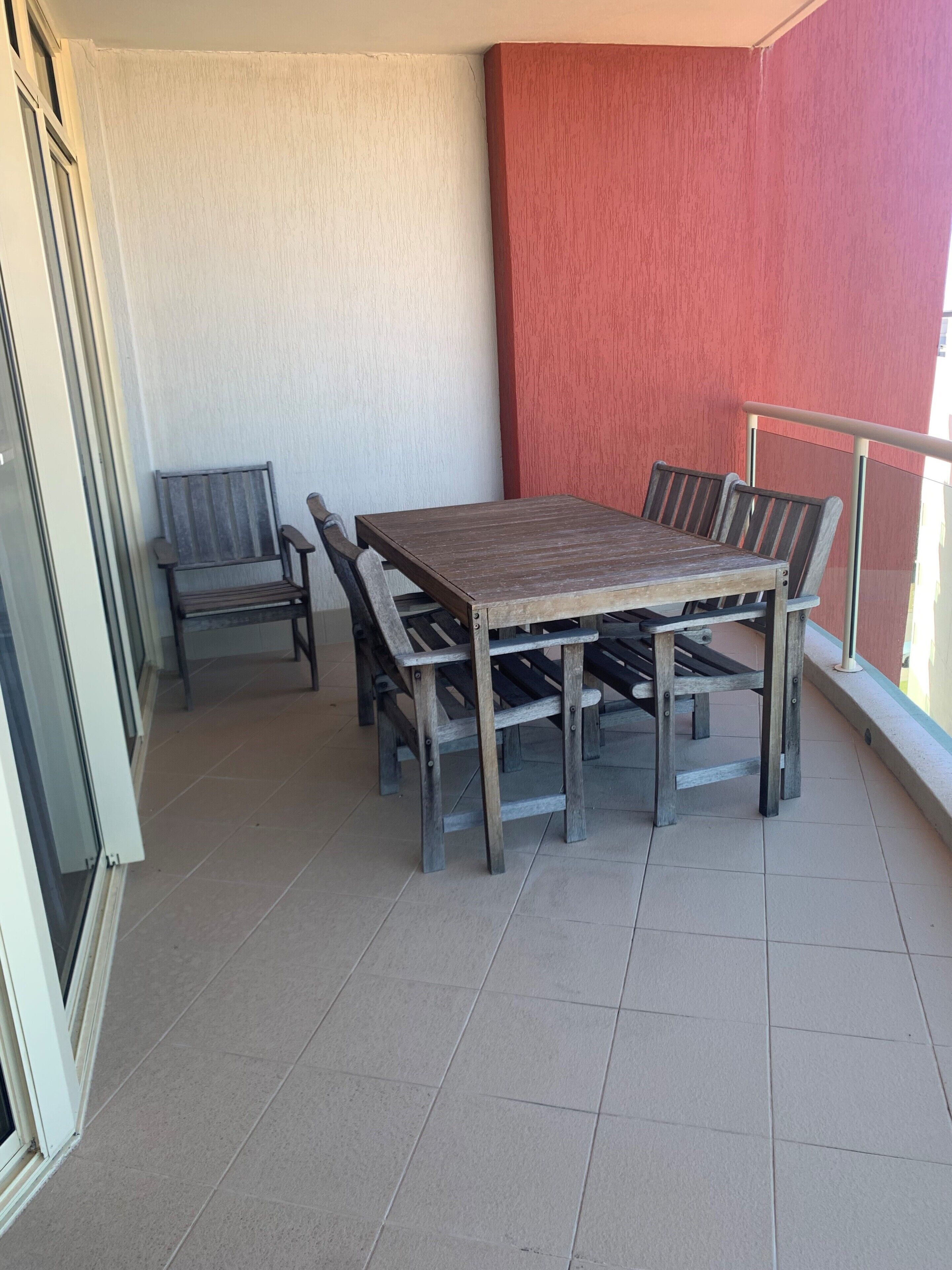 A balcony with a wooden table and chairs, a sliding glass door, and a red wall.
