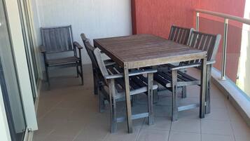 A balcony with a wooden table and chairs, a sliding glass door, and a red wall.