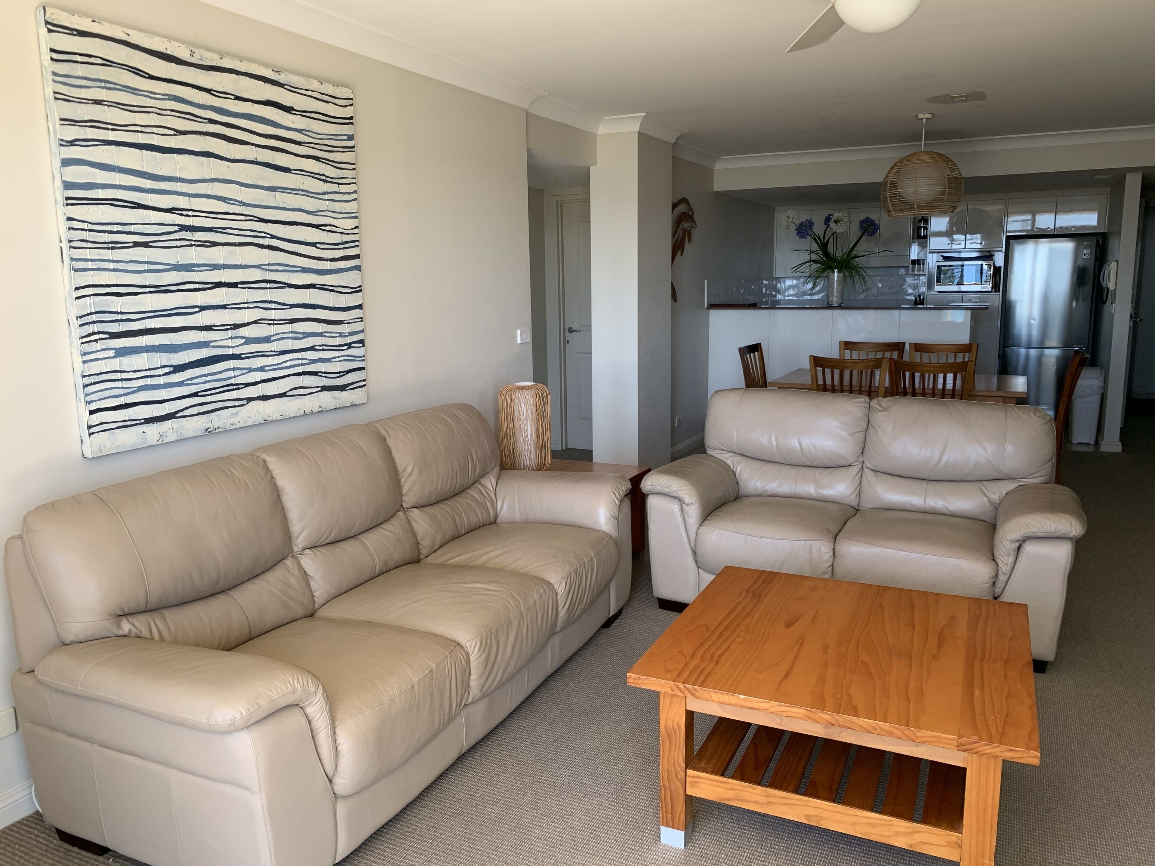 Ein Wohnzimmer mit einem beigefarbenen Ledersofa, einem Holztisch und einem modernen abstrakten Gemälde an der Wand.