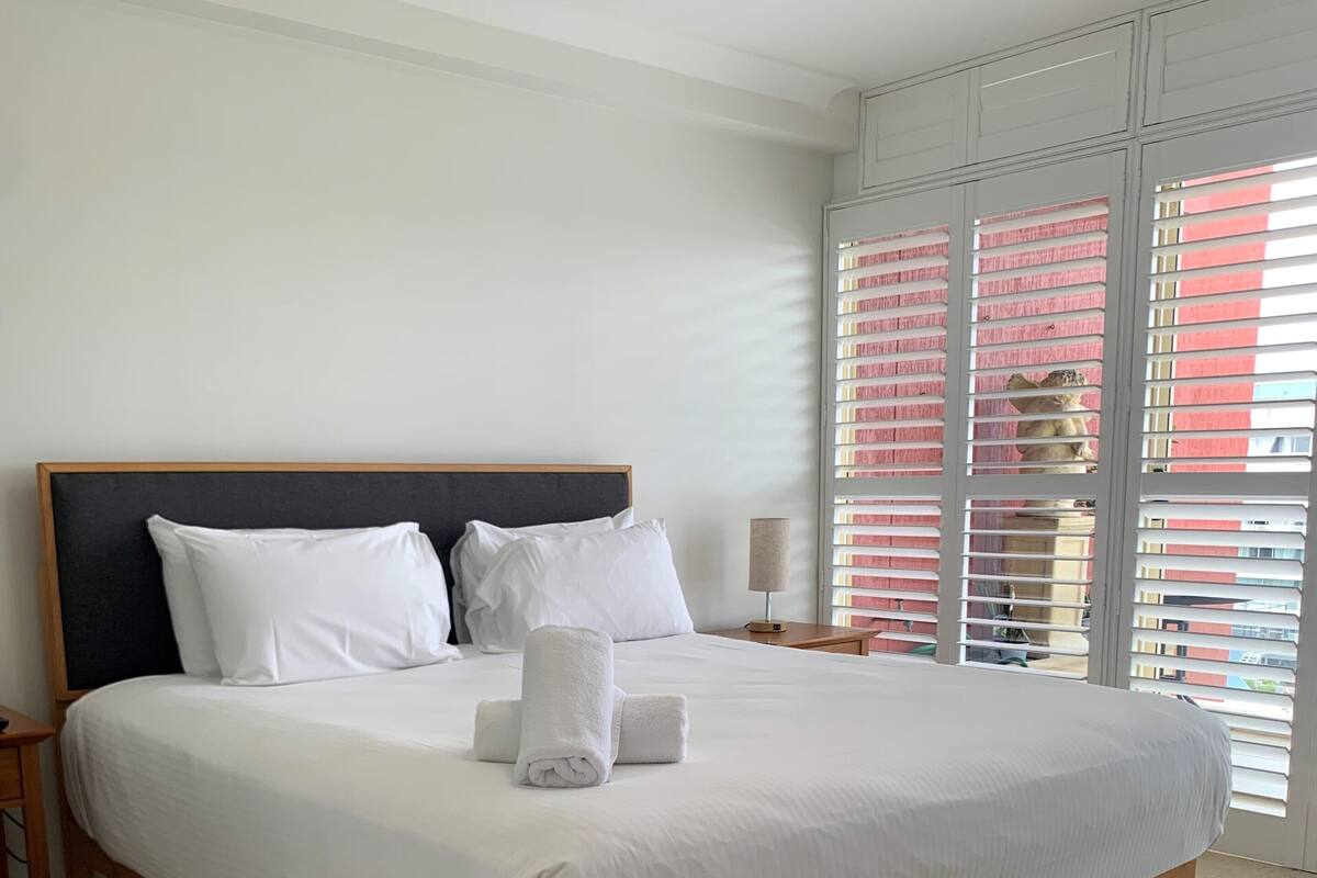 Una cama grande con ropa blanca, un cabecero de madera y una mesita de noche con una lámpara.