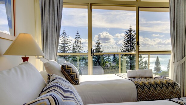 Une chambre d’hôtel avec deux lits, une grande fenêtre donnant sur des arbres et des montagnes, et une lampe sur le côté gauche.