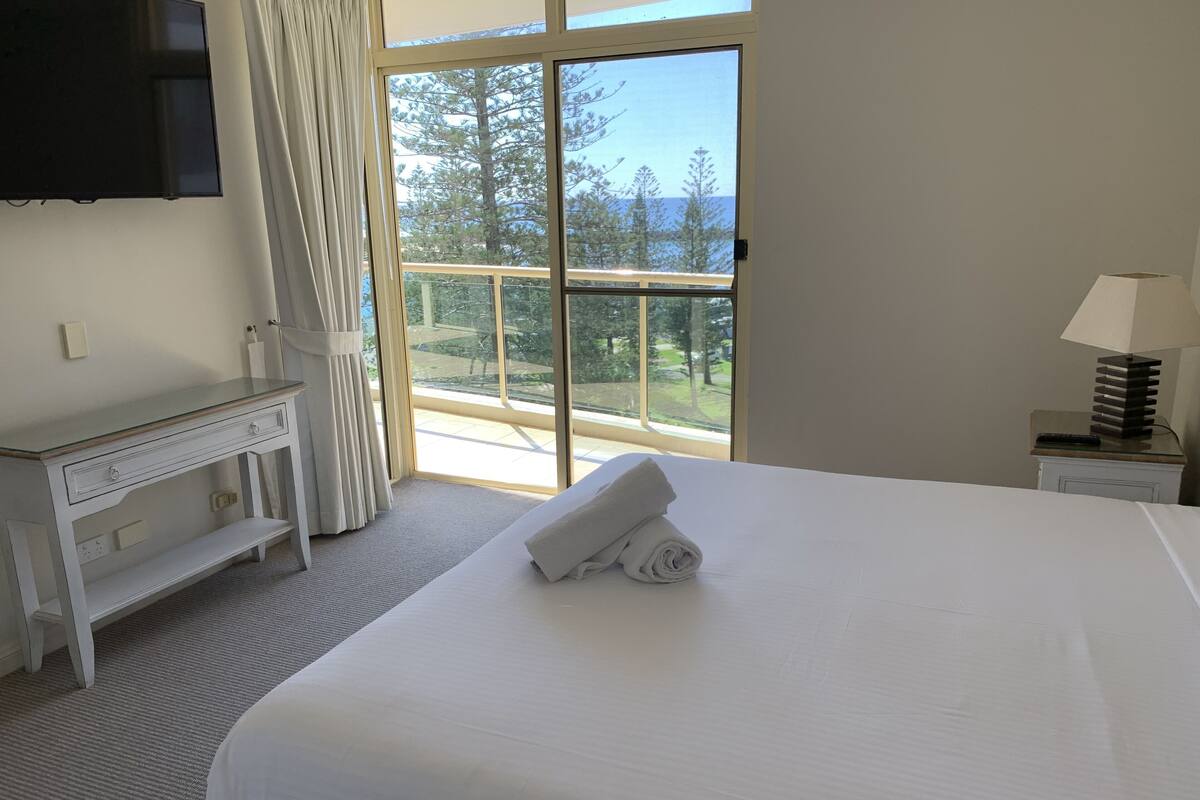 Habitación de hotel con una cama grande, un escritorio, un televisor y vistas a árboles a través de un ventanal corredera.