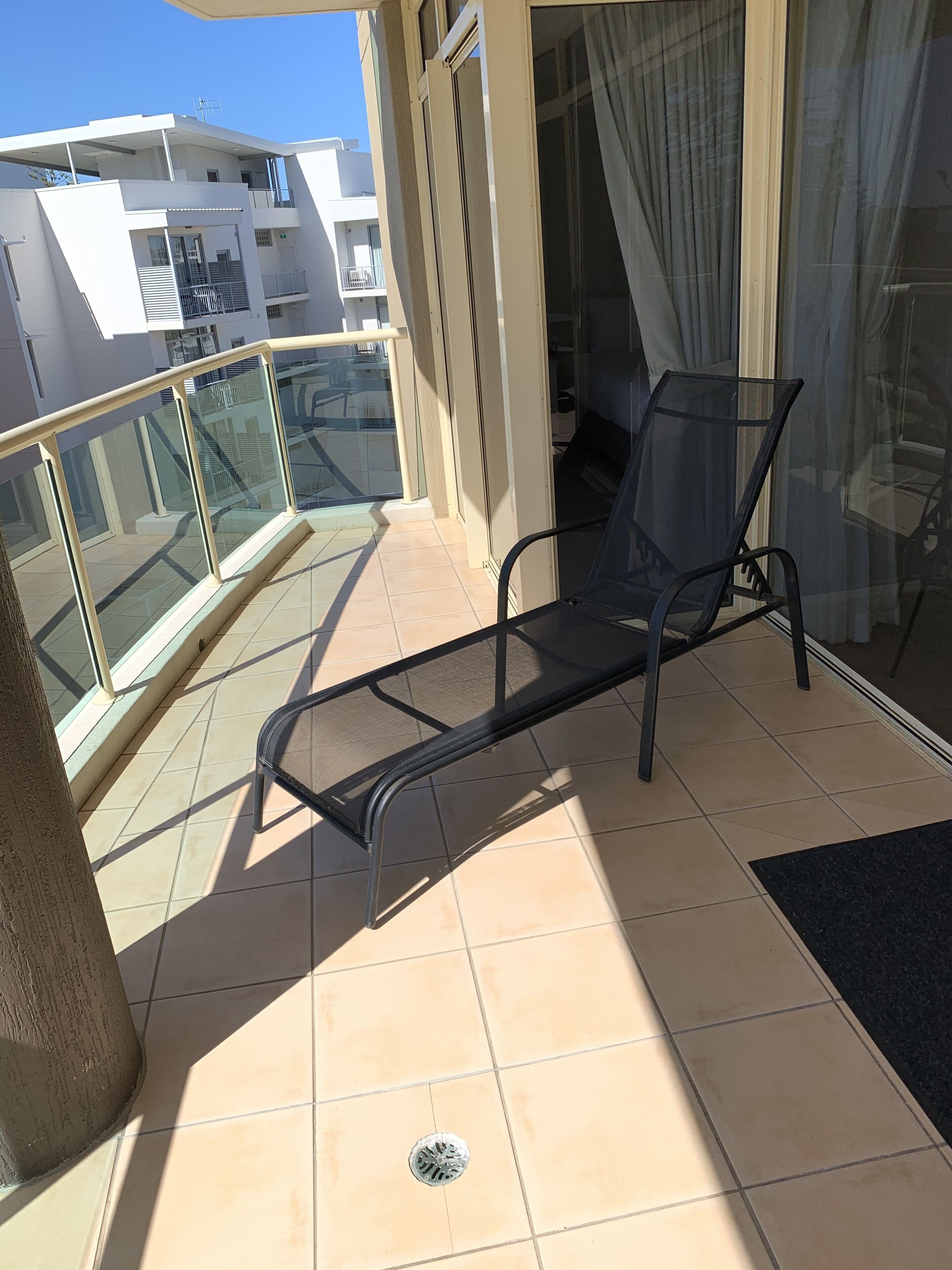 A balcony with a glass railing, a black metal chair, and a tiled floor.