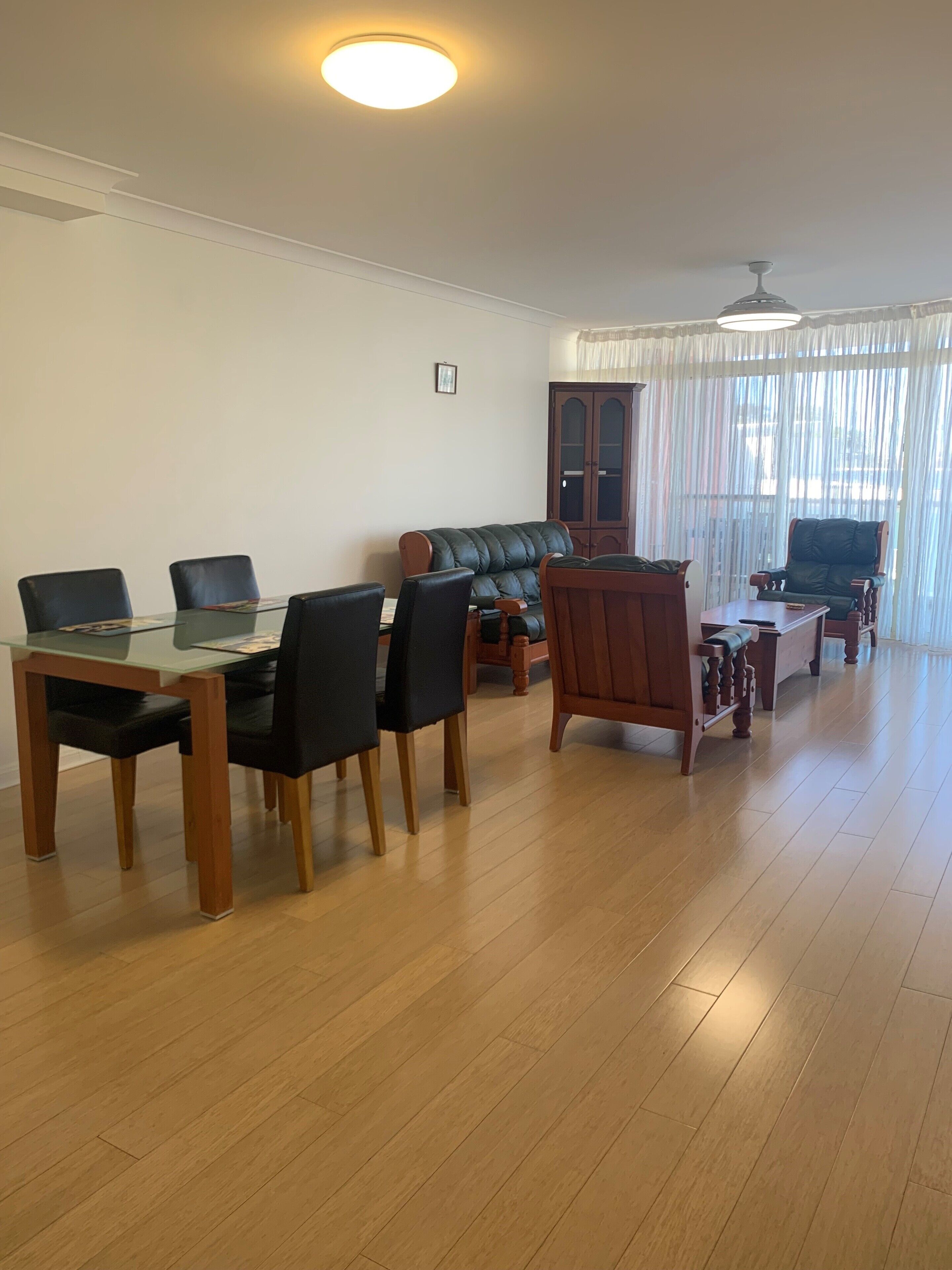 A spacious living room with a dining table, chairs, a sofa, and a wooden cabinet.