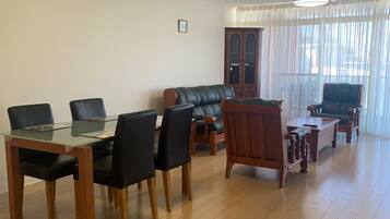 A spacious living room with a dining table, chairs, a sofa, and a wooden cabinet.