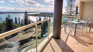 Un balcon donnant sur un lac et des arbres, une table avec des chaises et une rambarde en verre.