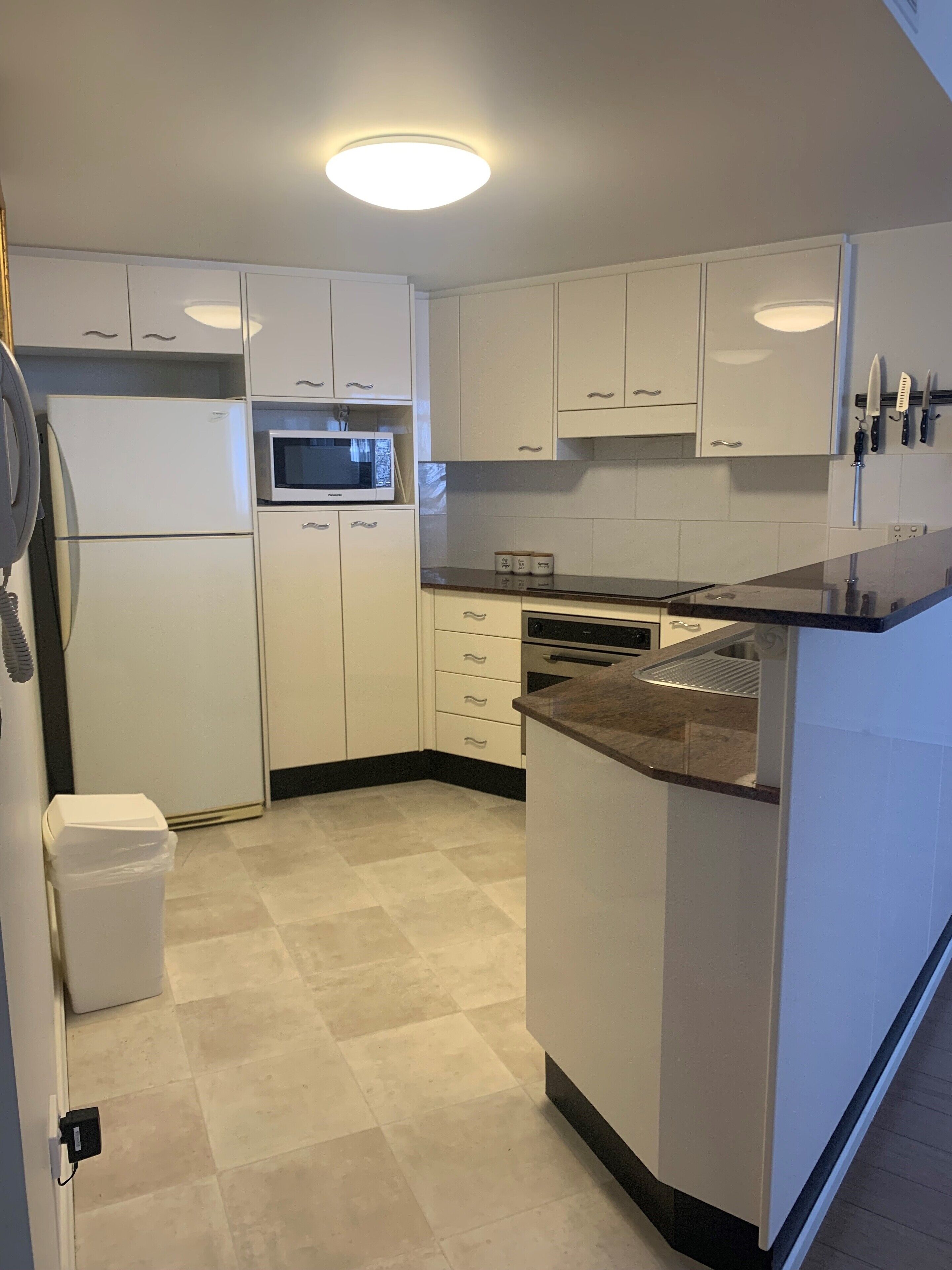 A modern kitchen with white cabinets, a microwave, a dishwasher, and a granite countertop.