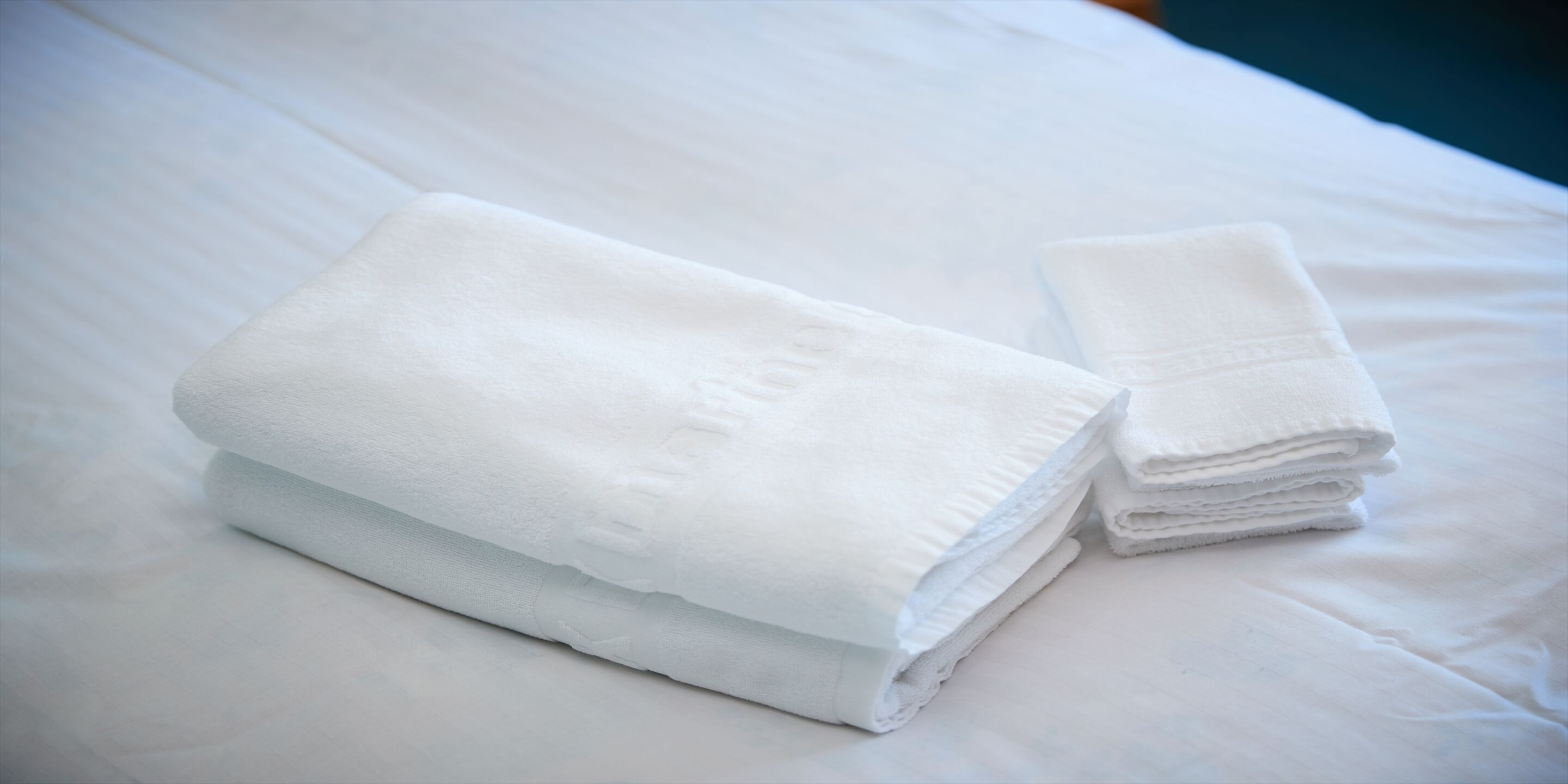 A neatly folded white towel on a bed with a smooth texture.