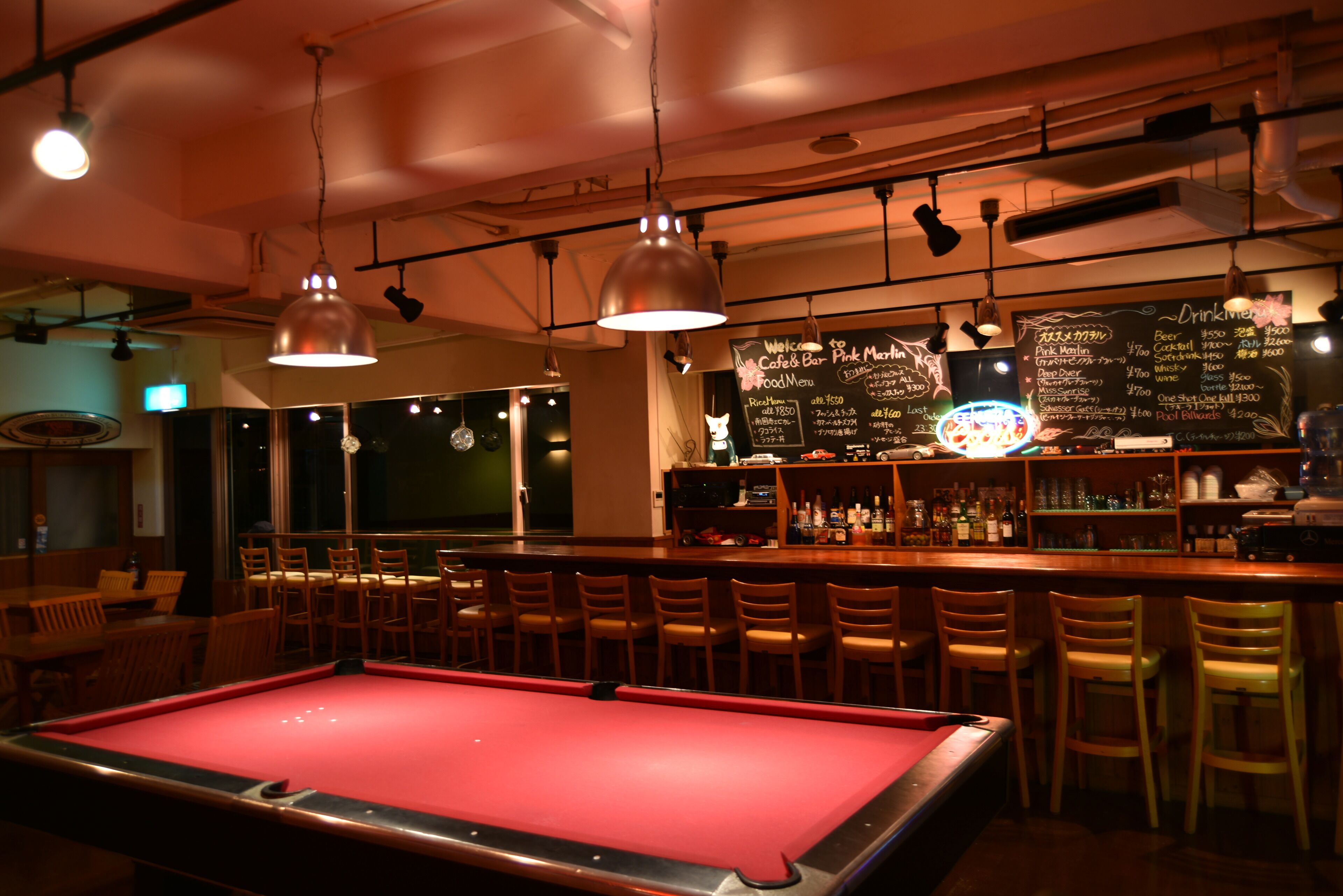 A bar area with a pool table, bar stools, and a chalkboard menu.