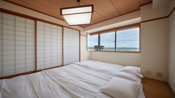 Quarto com cama, biombos deslizantes estilo shoji, janela com vista e luminária no teto.