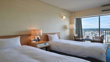 A hotel room with two beds, a desk, a chair, and a large window offering a view of the city.