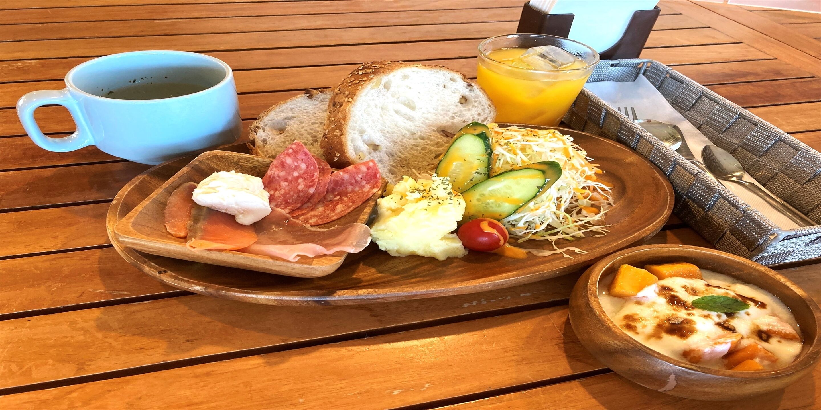 A breakfast tray with bread, cheese, cured meats, vegetables, and a bowl of fruit.