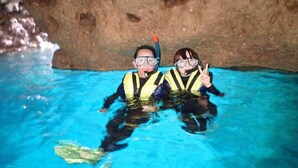Duas pessoas em uma piscina azul translúcida com paredes rochosas.