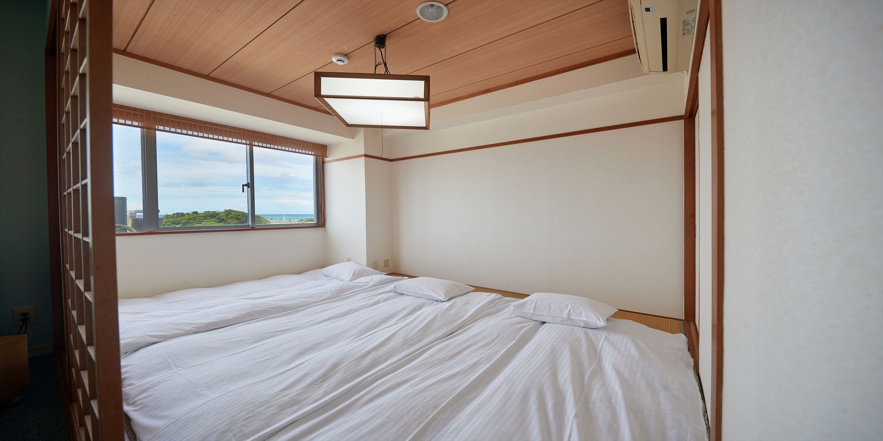 A single bed with white bedding in a room with wooden paneling and a large window.