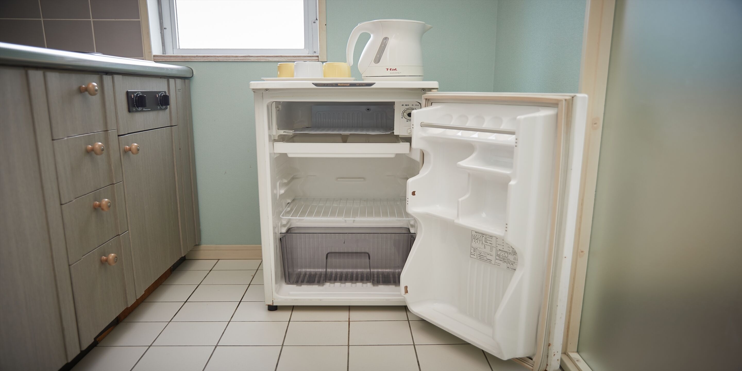 A kitchen with a refrigerator, a microwave, and a kettle on the countertop.