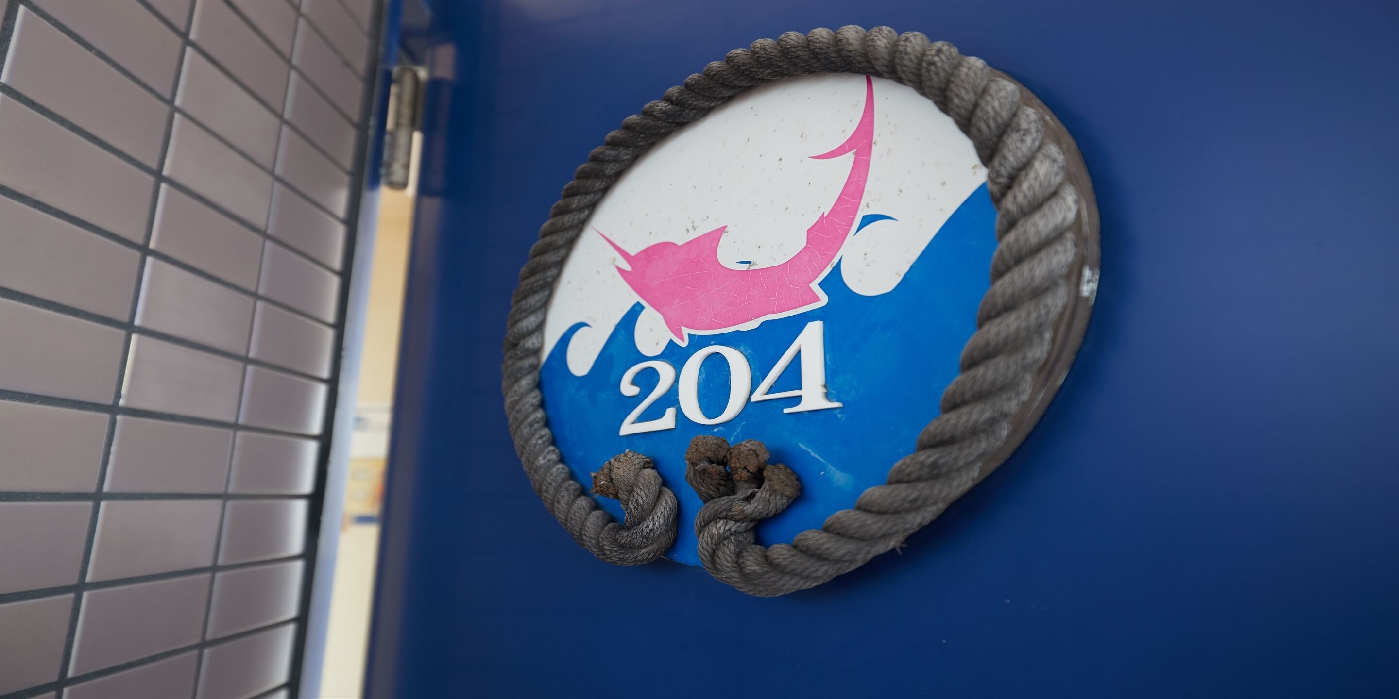 Un letrero montado en la pared con un borde de cuerda y un dibujo de un pájaro, que muestra el número 204.