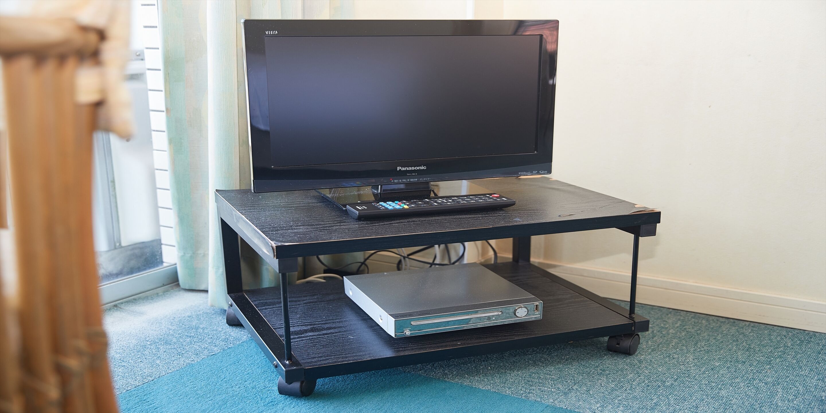 A black TV on a black TV stand with a remote control and a DVD player.