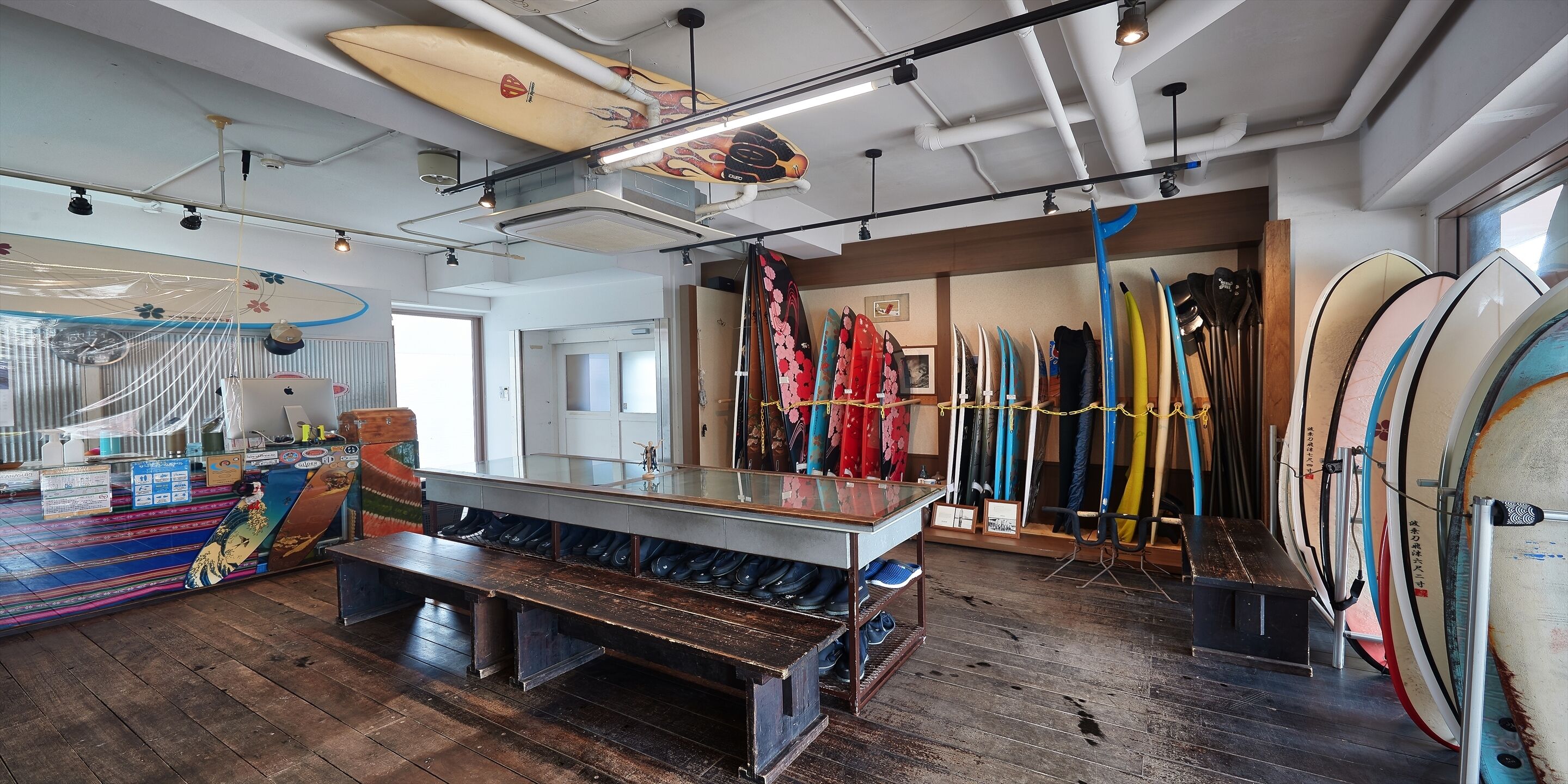 A surf shop interior with wooden floors, surfboards, and a glass display table.