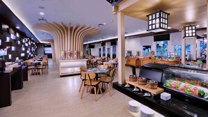 Un intérieur de restaurant moderne, avec plusieurs tables et chaises, un bar à sushis et un décor de plafond original.