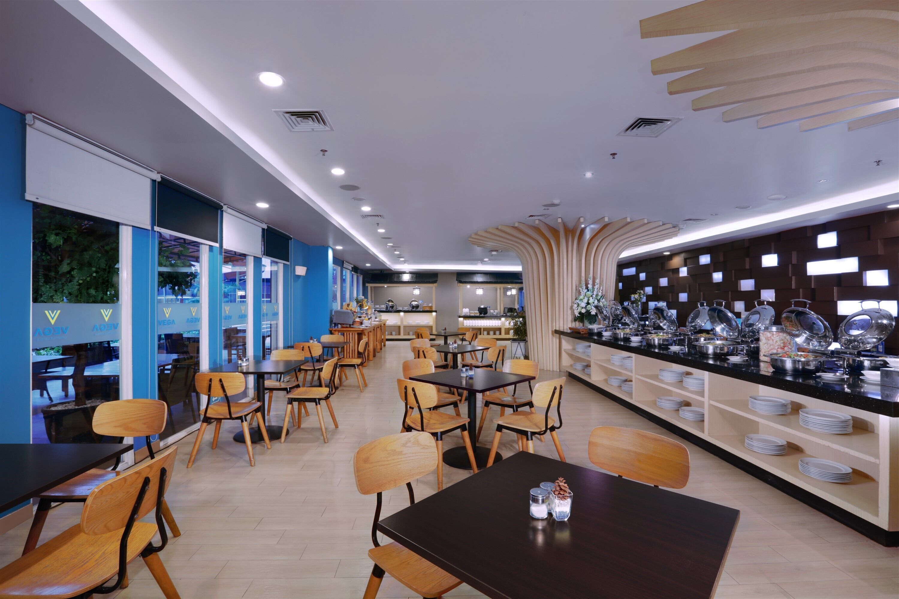 Un restaurante moderno con sillas y mesas de madera, una barra de buffet con platos, y una decoración en tonos azul y blanco.