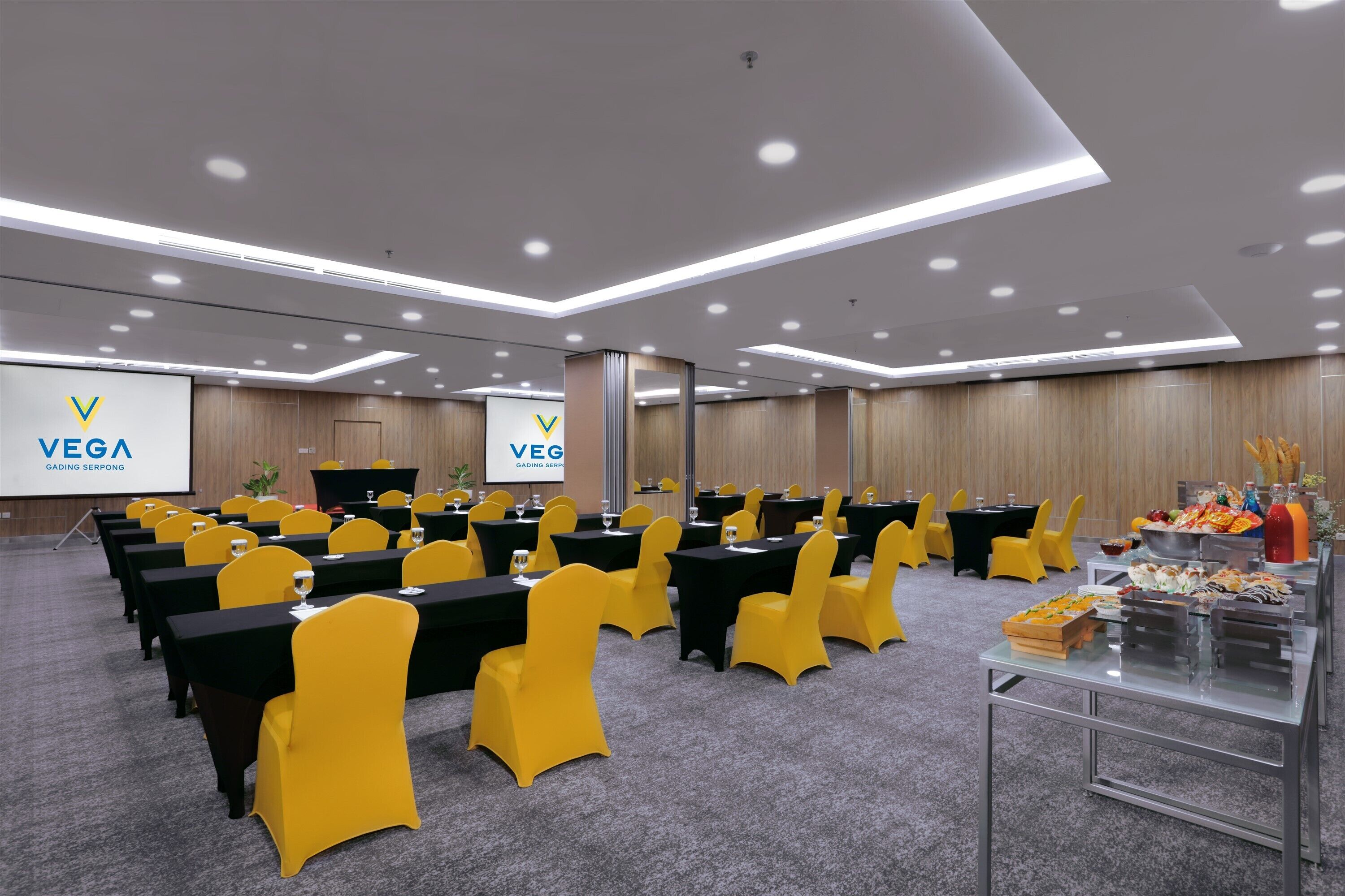 A conference room with rows of tables and chairs, a projector screen, and a buffet table with food.