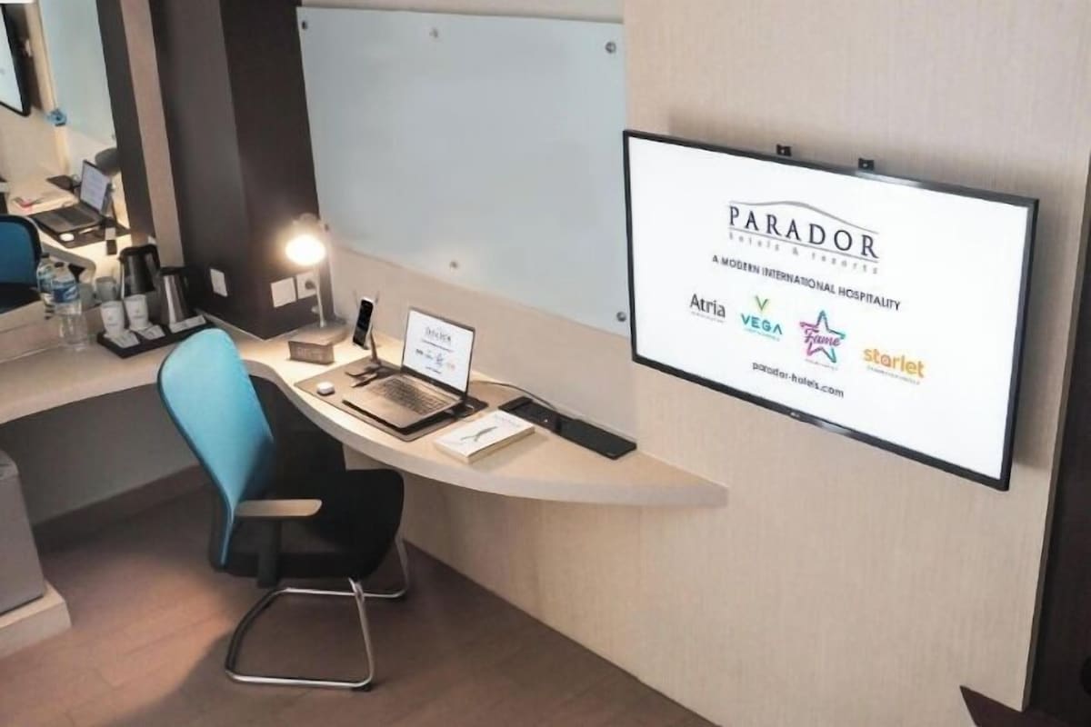 A modern hotel room with a desk, laptop, and a large screen displaying the hotel's name and partner brands.