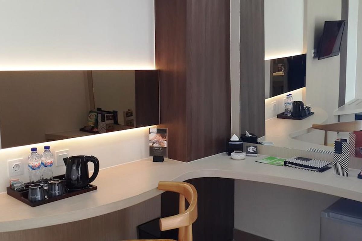 A hotel room with a curved desk, a chair, a coffee maker, water bottles, a TV, and a small shelf with snacks.