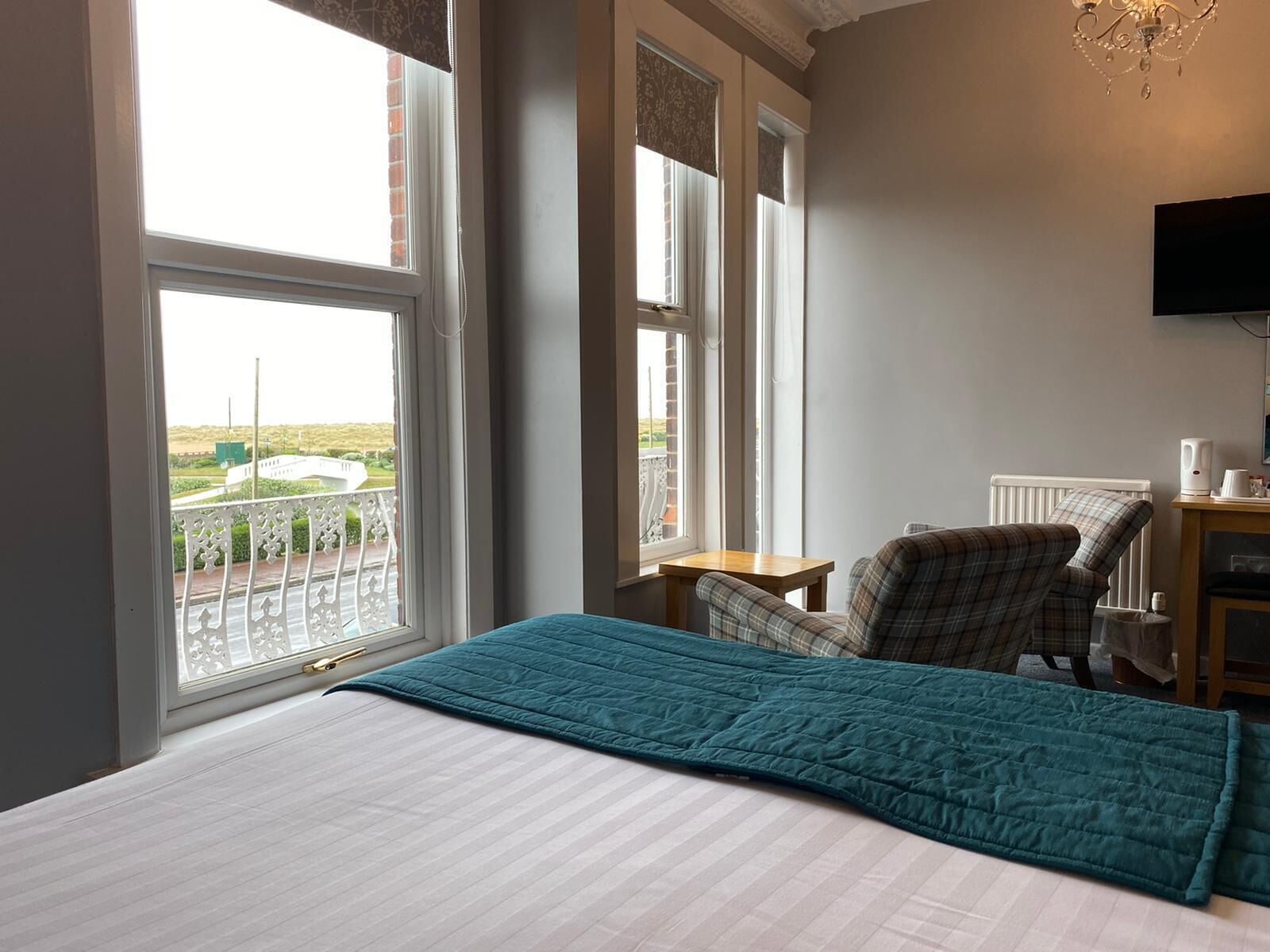 A hotel room with a bed, a chair, a small table, a TV, and a view of the outside.