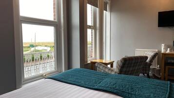 Ein Hotelzimmer mit Bett, Sessel, kleinem Tisch, Fernseher und Blick ins Freie.