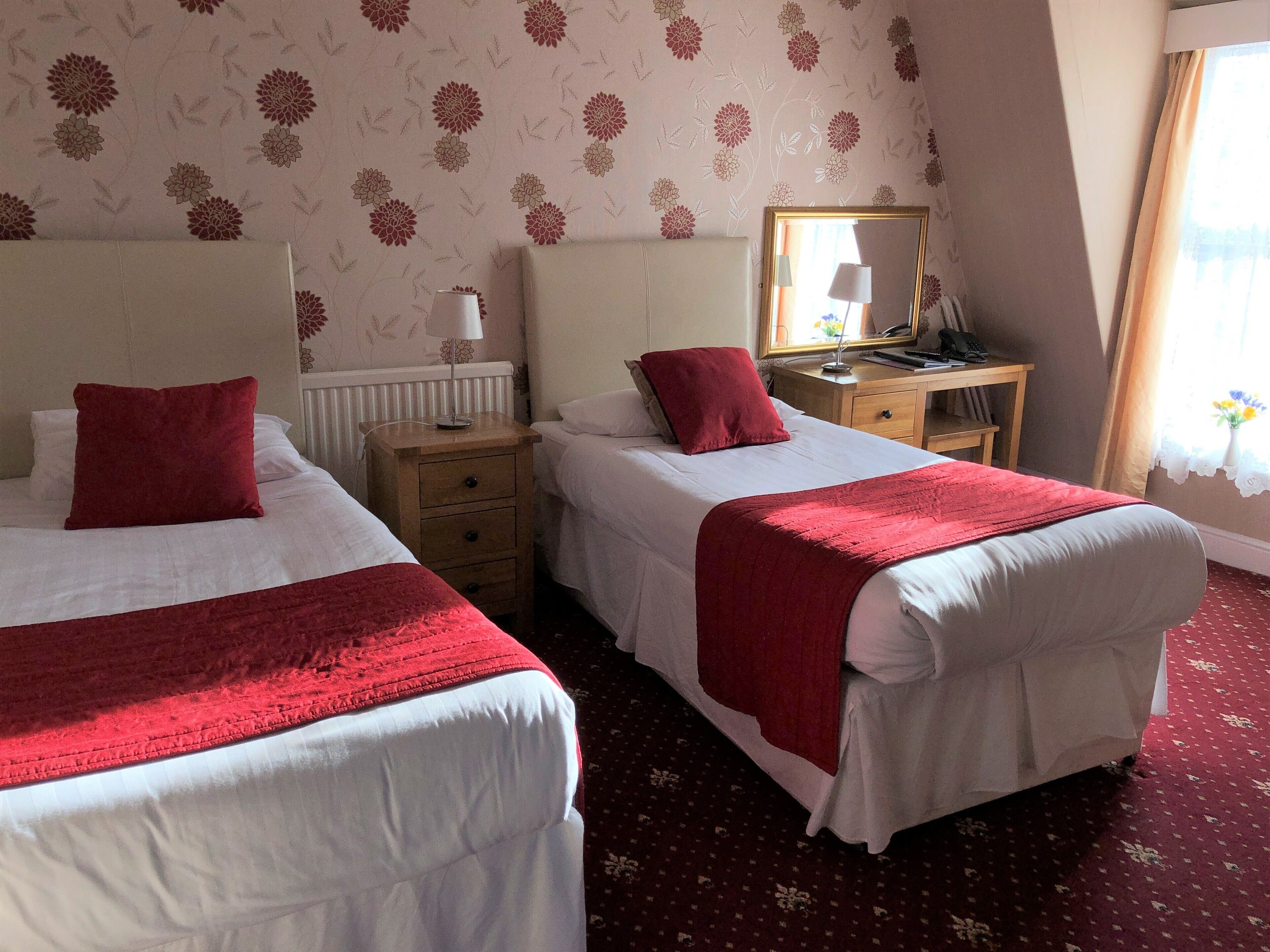 A hotel room with two beds, a desk, a mirror, and a window with curtains.