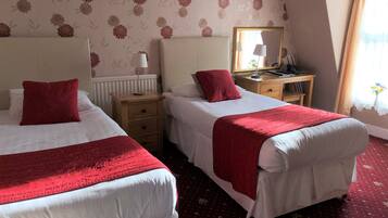 A hotel room with two beds, a desk, a mirror, and a window with curtains.