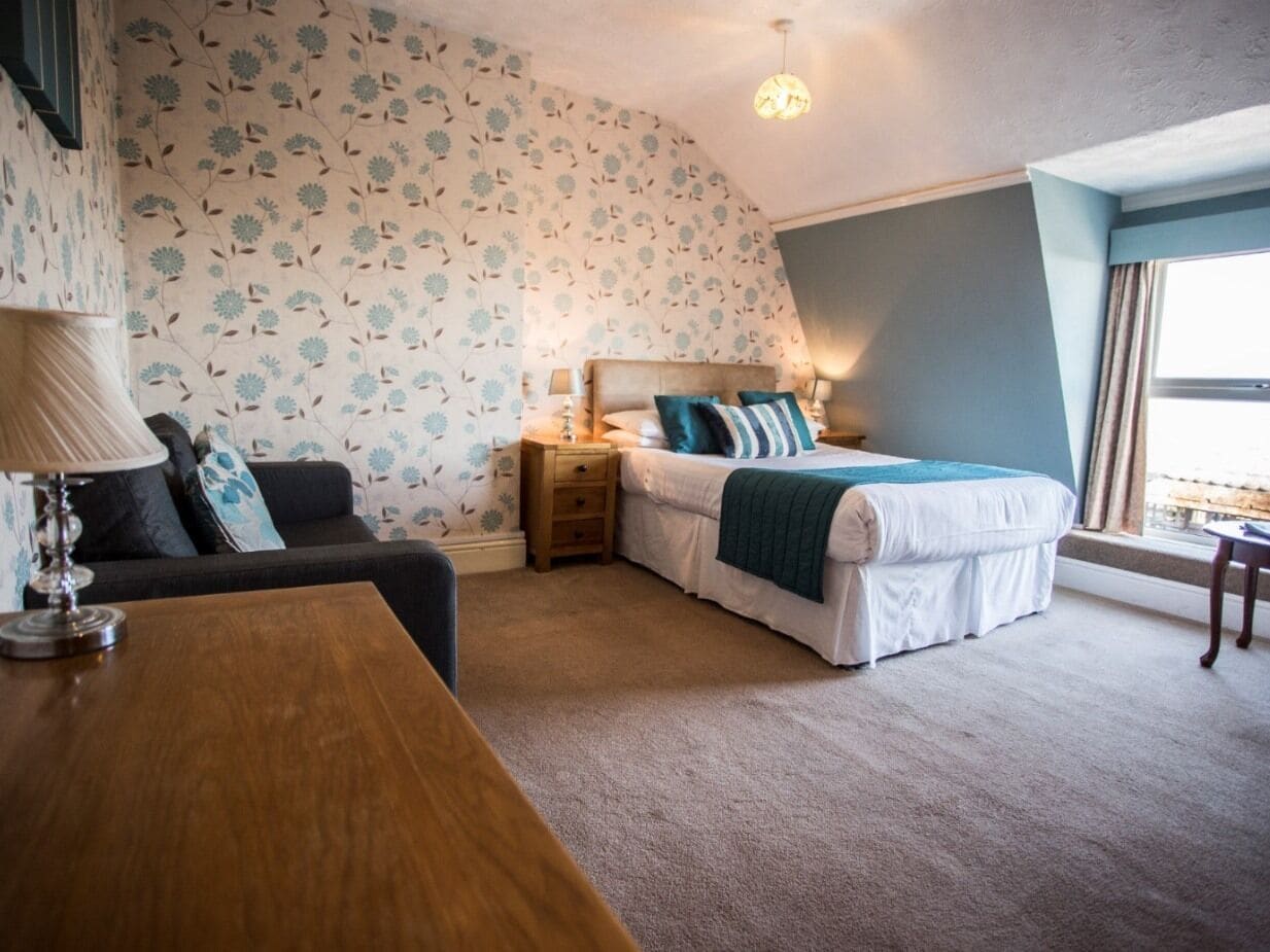 A bedroom with a bed, bedside tables, a desk, and a window.
