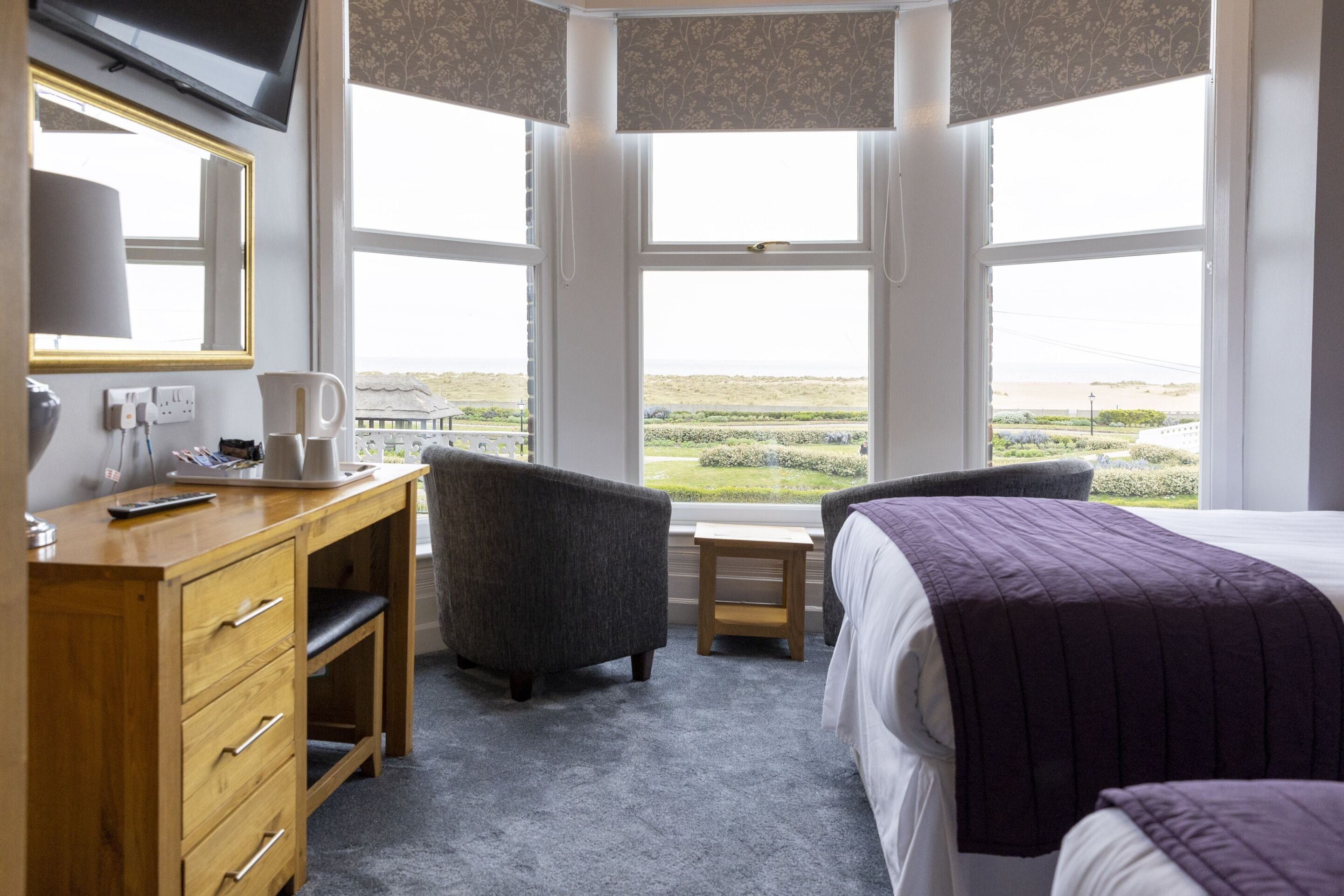 A hotel room with a desk, two chairs, a bed, and a large window offering a view of the landscape.