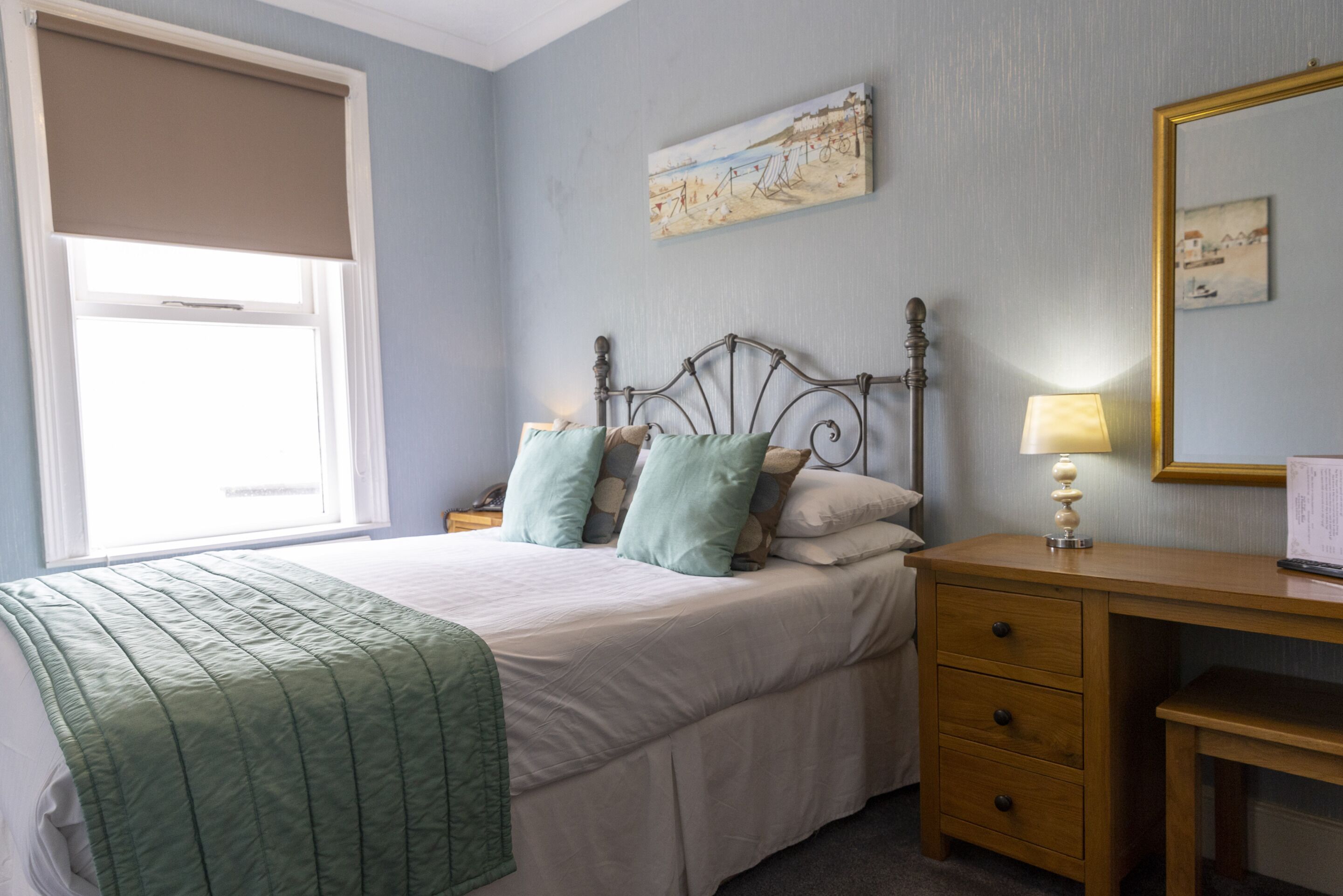 A bedroom with a bed, a nightstand, a wooden dresser, and a window with a beige blind.