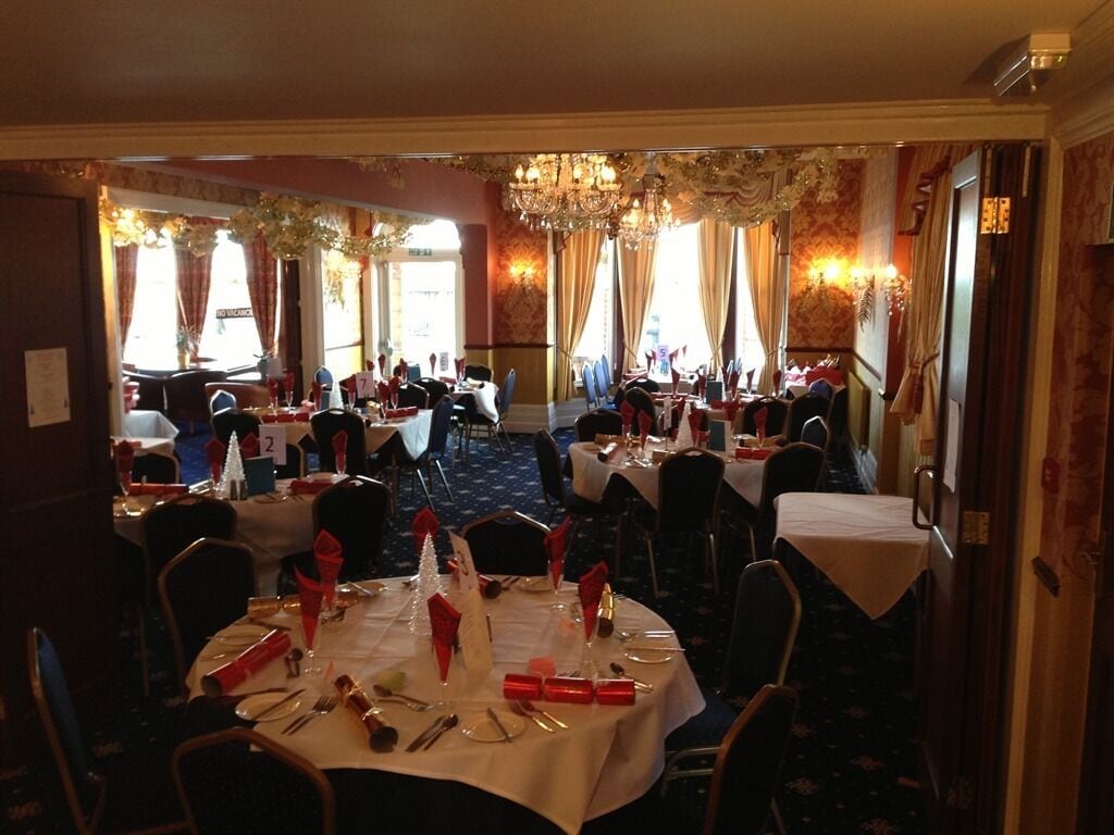 Ein Bankettsaal mit runden Tischen, die für das Essen gedeckt sind, Stühle um jeden Tisch herum und einer Kristallleuchter, der von der Decke hängt.
