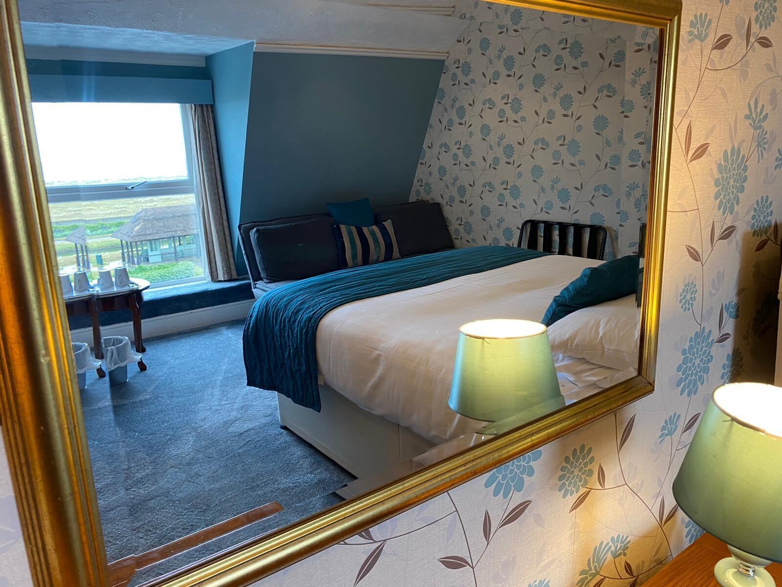 A bedroom with a bed, a nightstand, a lamp, a window with a view, and a mirror.