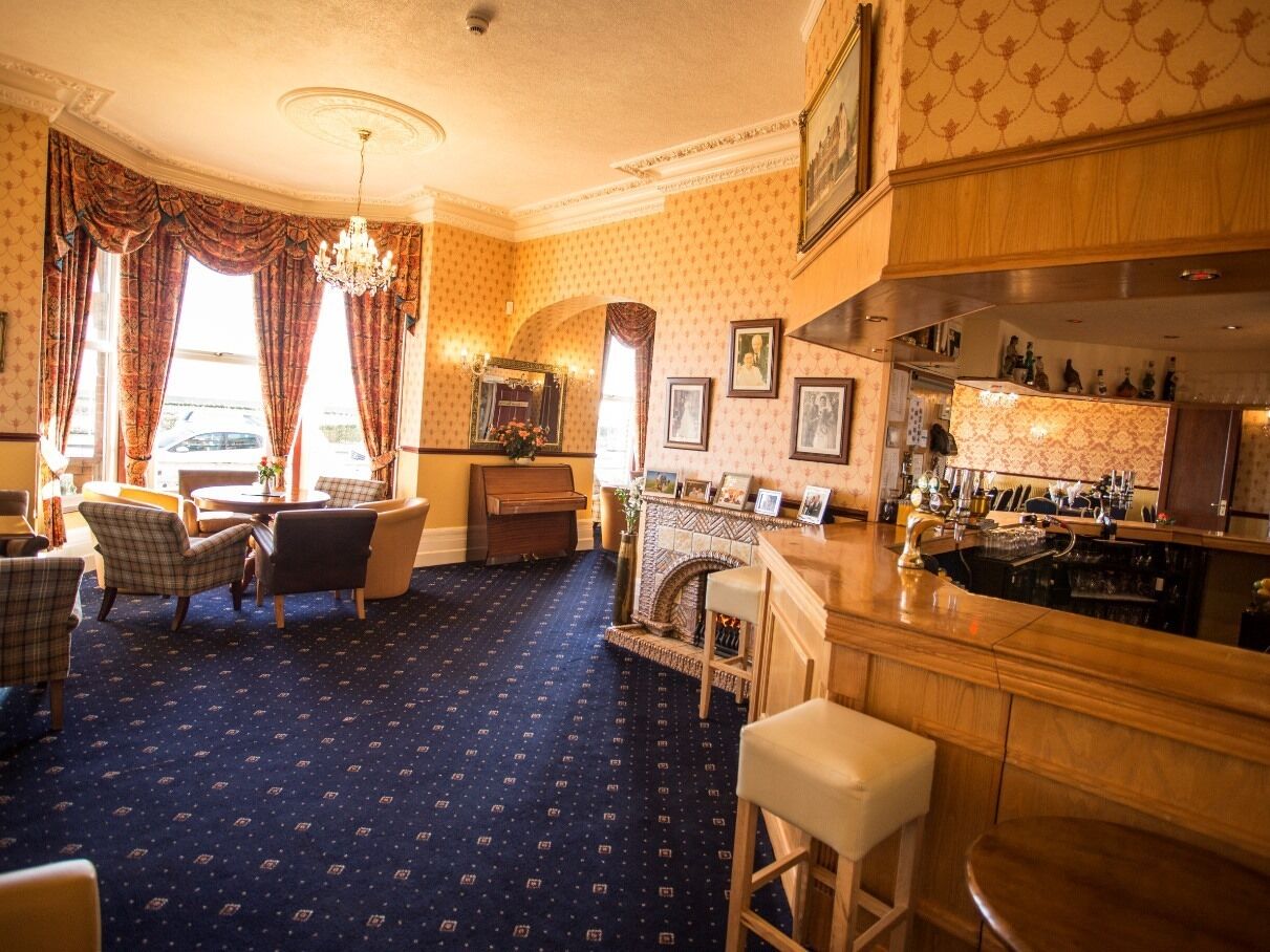 A room with a bar area, seating, a fireplace, and a patterned carpet.