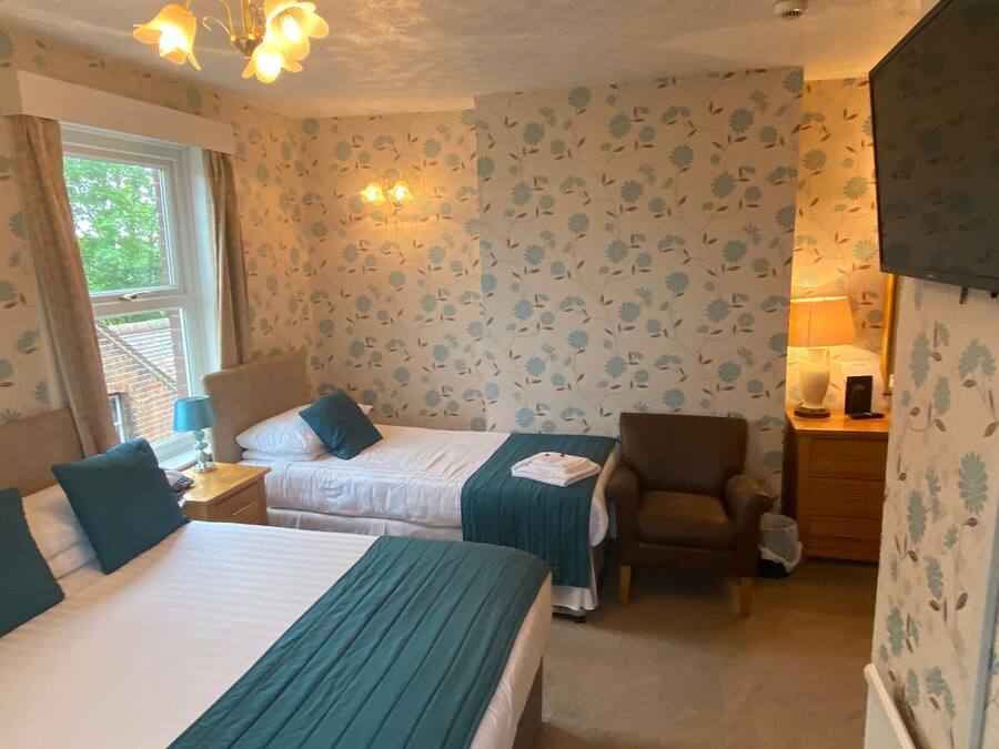 A hotel room with two beds, a chair, a nightstand, and a lamp.