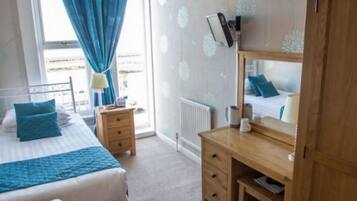 A bedroom with a bed, a wooden desk, a mirror, a radiator, and a window with curtains.