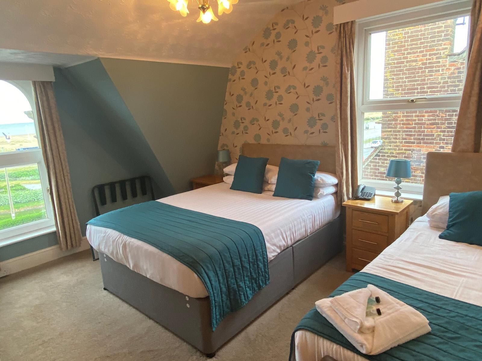 A bedroom with two beds, a window with a view, a bedside table with a lamp, and a radiator.