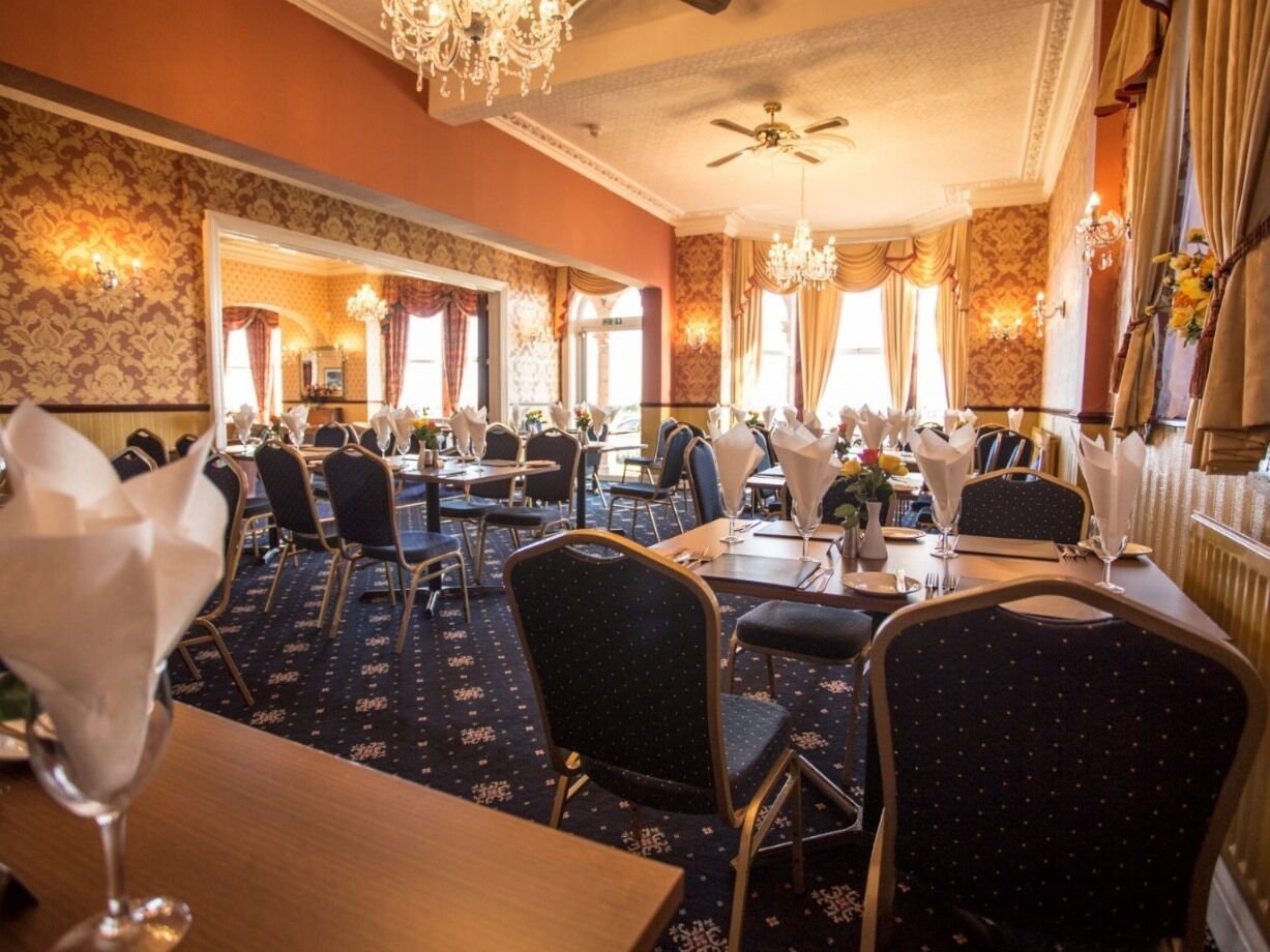 A formal dining room with multiple tables and chairs, a chandelier, and a ceiling fan.