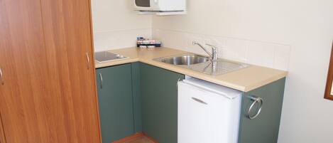 Una cocina compacta con un refrigerador blanco, un microondas y un lavamanos.