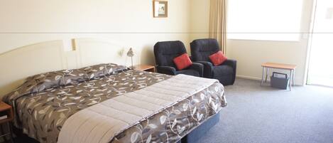 Une chambre d’hôtel avec un grand lit, deux fauteuils, une petite table et une fenêtre avec des rideaux.